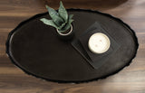Oval-shaped dark tray with a subtly scalloped edge resting on a wood surface, featuring a small potted plant with textured leaves and a white two-wick candle on black coasters.