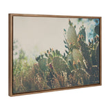 Framed canvas of a desert prickly pear cactus bathed in soft sunlight with blurred green foliage in the background, highlighting the cactus' pads and spines.