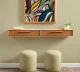 Wall-mounted wooden console table with two drawers, paired with two beige round ottomans beneath and a vibrant abstract leaf artwork above in soft green wall setting.