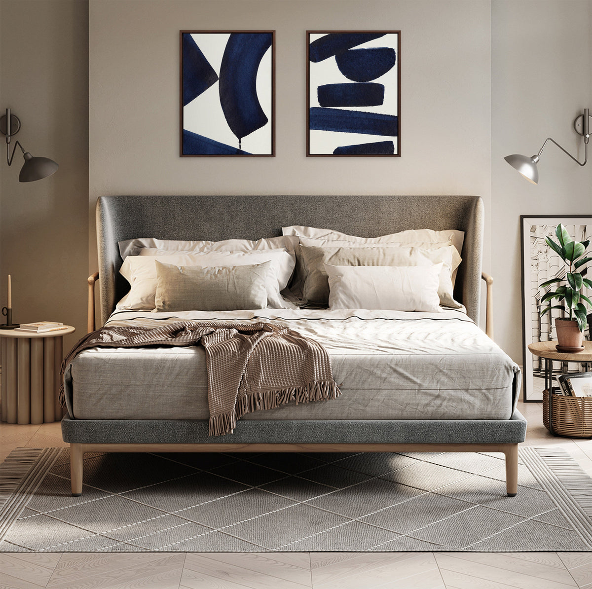 Modern bedroom with gray upholstered bed, beige bedding, two abstract navy blue and white framed artworks above the headboard, and pendant lamps on each side.