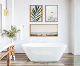 Modern bathroom with a white freestanding bathtub centered on wood-patterned floor tiles, featuring three framed nature-themed artworks above it.