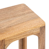 Close-up of a square wooden tea table corner with smooth rounded edges and visible natural wood grain texture in light brown tones.