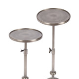 Two round polished metal plant stands with adjustable heights, featuring flat circular tops and wing nut clamps on vertical cylindrical supports.