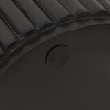 Close-up of a black cylindrical wooden object with vertical grooves and a small round black felt pad on the flat end surface.