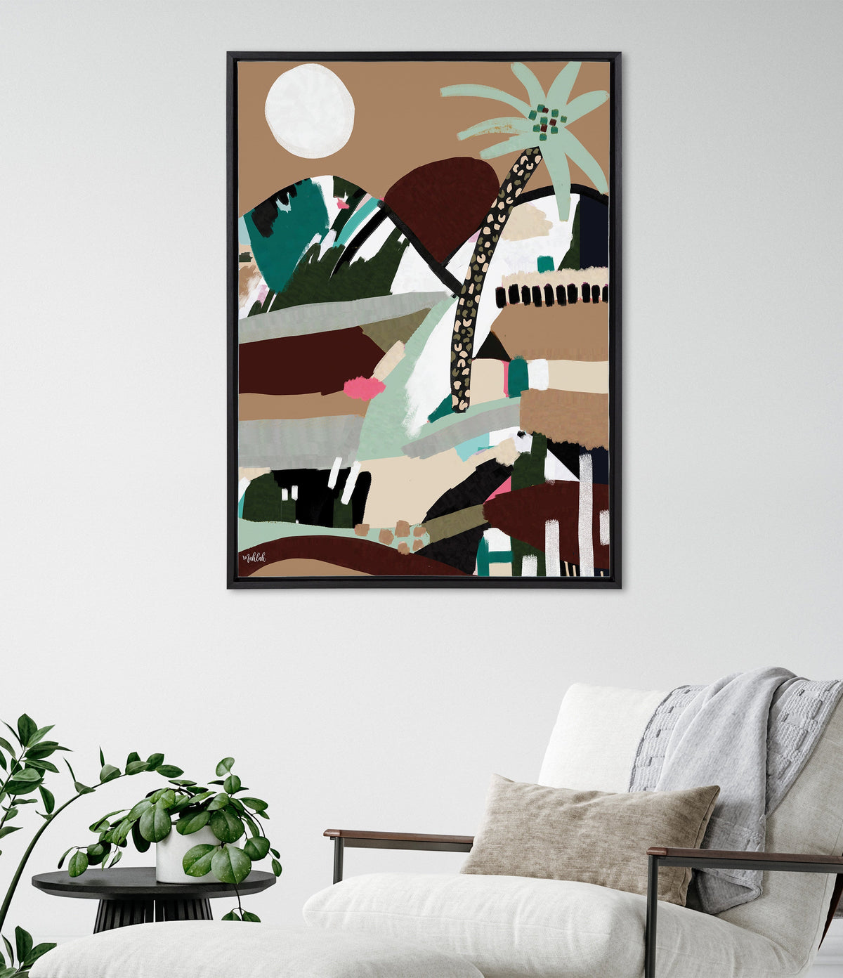 Abstract framed canvas with a large white circle, green and brown shapes, and a stylized tree with a spotted trunk against a tan background, hanging above a white chair.