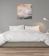 Sepia-toned framed canvas featuring a cloudy sky over a muted landscape, displayed above a bed with white bedding against a gray wall.