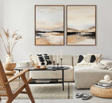 Modern living room with cream sectional sofa, black-and-white patterned pillows, two neutral-toned abstract landscape paintings in wooden frames, and a wooden chair with woven seat.