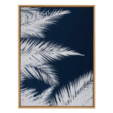 Framed canvas artwork featuring white palm leaf silhouettes against a deep navy blue background, arranged in a layered, overlapping composition.