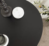 Top view of a round black wood side table with a matte finish, featuring a black candlestick and two white marble coasters, next to a green potted plant.