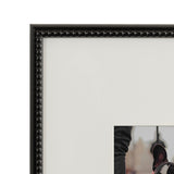Close-up of a black photo frame with rounded bead detailing along the inner edge, surrounding a white mat with an opening showing a black and white dog's ear and neck.