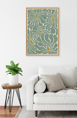 Abstract floral canvas with flowing pale green petals and mustard yellow centers in a light wood frame, hanging above a white sofa with beige cushions and a small wooden side table with a green potted plant.