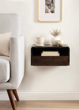 Dark wood floating side table mounted on white wall beside light gray sofa, holding a cream mug, small vase with dried flowers, and a cup, with books stored below.