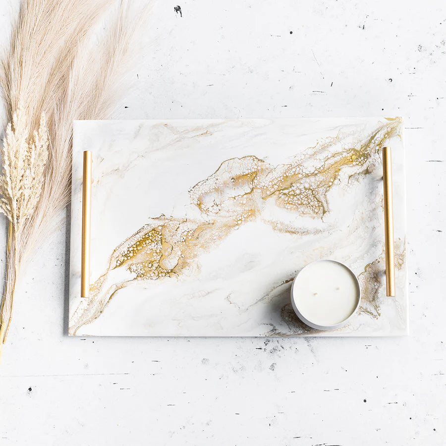 Marble-patterned Acrylic Resin Serving Tray with gold accents on a white surface with a candle and dried plants.