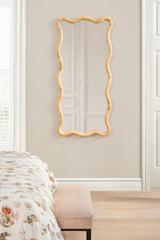 Tall rectangular wall mirror with scalloped edges framed in curved natural rattan, hanging on a beige bedroom wall above a cushioned bench.