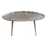 Oval metal coffee table with a textured surface and scalloped, uneven edges supported by three tapered legs in matching metal finish.