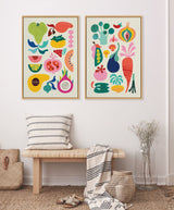 Two framed canvas prints featuring colorful abstract fruit and vegetable illustrations in various shapes and bright hues, hung above a wooden bench with striped pillows and throws in a minimalist room.