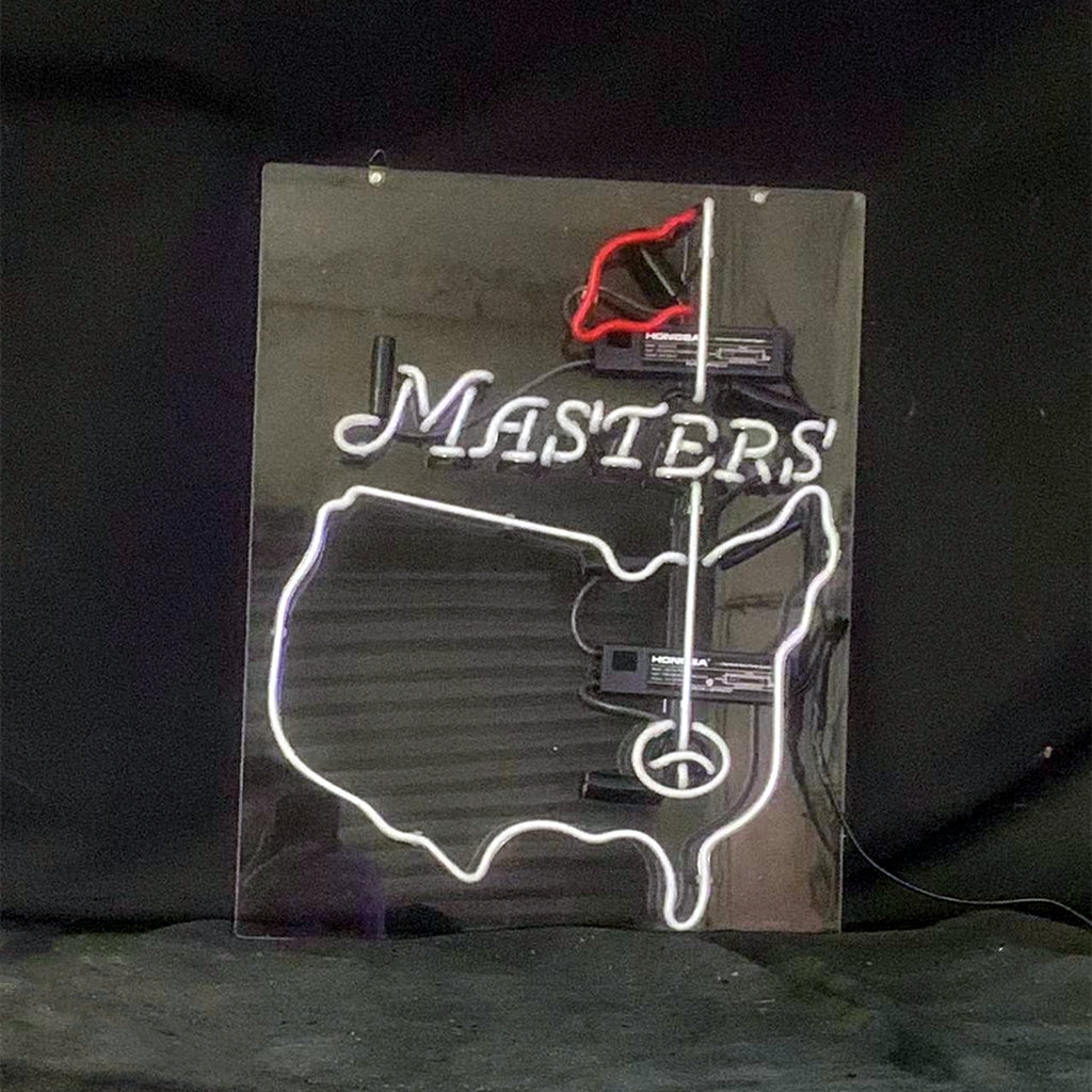 Neon sign on black background showing a white outline of the USA with a red flag and the word 'MASTERS' in white letters above a golf hole design.