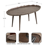 Oval coffee table with a scalloped metal tabletop featuring sand-cast texture and tapered wooden legs, measuring 33.5 by 20 by 14.75 inches.