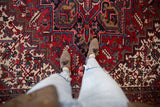 Person wearing leopard-print shoes and light blue jeans stands on a richly patterned red, white, and black Mehrivan carpet with geometric and floral motifs.