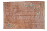Rectangular vintage Japanese Art Deco carpet in muted rusty brown with floral sprays in soft cream, peach, and green near top right and bottom left corners, fringed edges.
