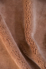 Close-up of a brown textured fabric with soft, raised, and curled fibers creating wavy folds and a plush, furry feel.