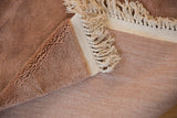 Close-up of a vintage Japanese Art Deco carpet showing its soft beige woven surface with delicate white fringe and a folded corner revealing a plush textured backing in a warm brown tone.