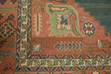 Close-up of a vintage Serapi Indian Soumac carpet corner featuring coral, green, blue, and beige geometric floral patterns with a detailed multi-layered border design.