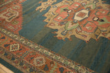 Vintage Serapi carpet with a large central floral medallion in muted red, green, and beige on a teal-blue background, featuring geometric and floral border patterns.