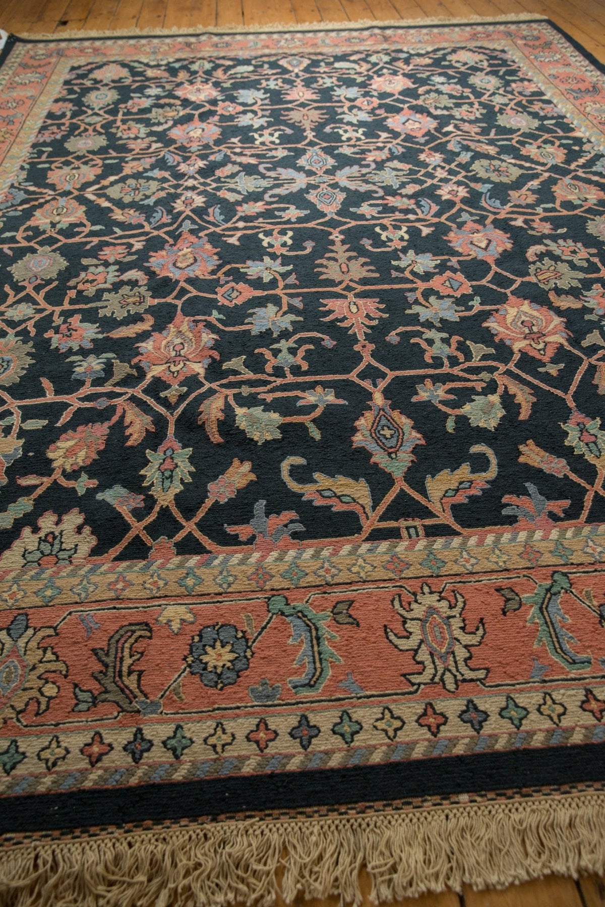 Vintage Serapi rug with a dark background, featuring intricate floral motifs in muted reds and greens and a wide terracotta border with symmetrical floral patterns.
