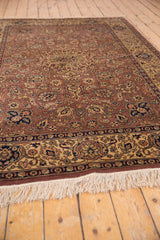 Rectangular vintage Romanian Tabriz carpet with intricate floral and medallion patterns in muted reds, blues, and golds, bordered by a decorative band and white fringe on wooden floor.