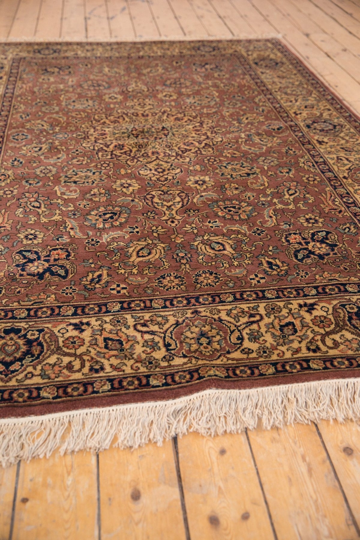 Rectangular vintage Romanian Tabriz carpet with intricate floral and medallion patterns in muted reds, blues, and golds, bordered by a decorative band and white fringe on wooden floor.