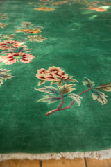 Green carpet with detailed floral patterns in pink, yellow, and beige, showing a close-up of flower stems and leaves along one edge with white fringe.
