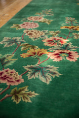 Green vintage carpet with a pattern of large, colorful flowers and leaves in shades of pink, red, yellow, and green arranged along a vertical stem on plush fabric.