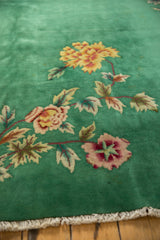 Green carpet with floral patterns featuring yellow and red flowers and green leaves, shown close-up with a tasseled edge on wooden flooring.