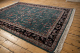 Rectangular 6x9 vintage Indian Mohajeran Sarouk carpet with teal blue center, intricate floral patterns, black and beige borders, and white fringes on natural wood floor
