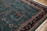 Teal vintage Indian Mohajeran Sarouk carpet with intricate floral and geometric motifs, bordered by a black band featuring pink and beige flower patterns, on wooden floor.