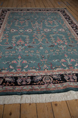 Rectangular vintage Mohajeran Sarouk carpet with teal field, intricate floral and geometric motifs in pink, cream, and black border, laid on wooden floor.