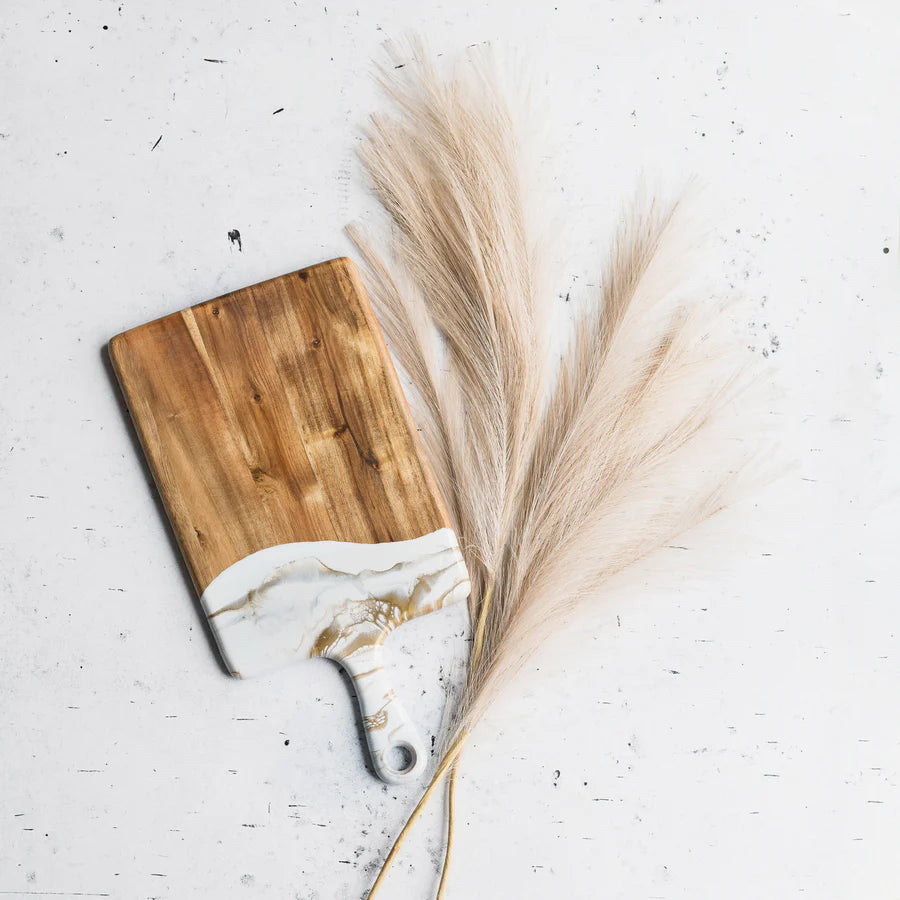 Wooden resin charcuterie board with marble design handle and dried pampas grass on a light background