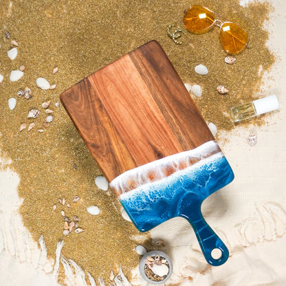 Wooden resin charcuterie board with blue resin edge on a sandy background