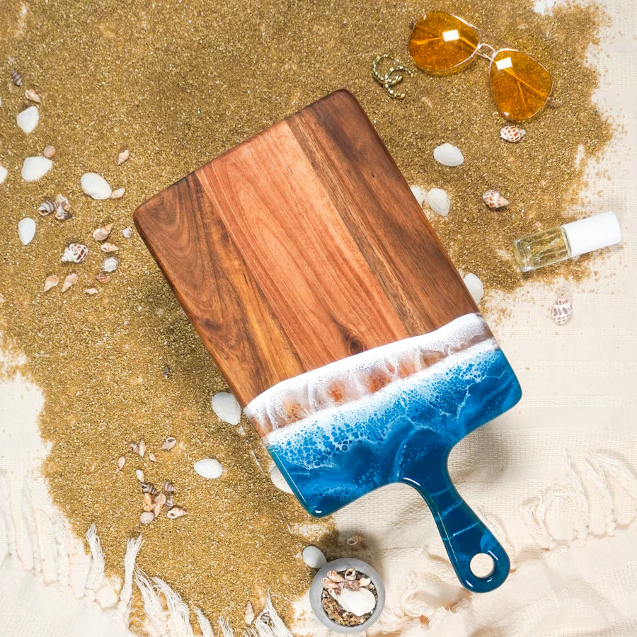 Wooden resin charcuterie board with blue resin edge on a sandy background