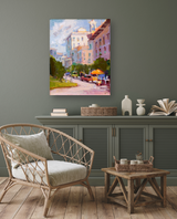 Impressionist-style painting of a sunlit city street with pastel buildings, green trees, and warm yellow-orange umbrellas on a cloudy midday.