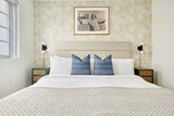 King-size bed with beige upholstered headboard, white bedding, two indigo blue patterned pillows, and textured beige throw, flanked by dark wood nightstands with rattan drawers.