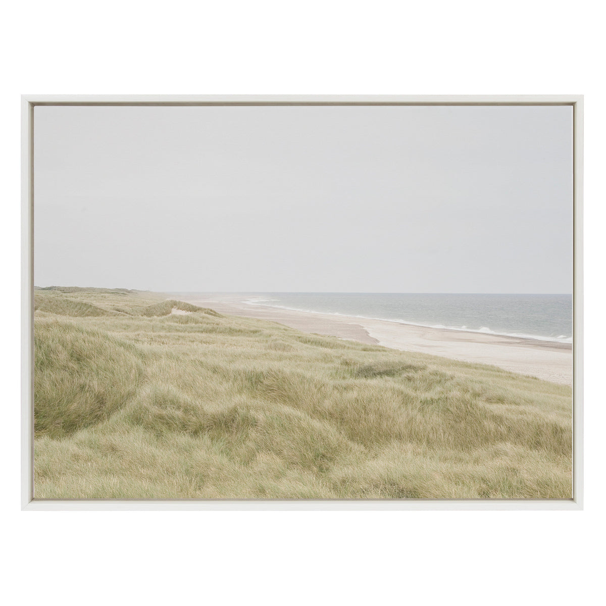 Framed canvas showing a serene coastal landscape with soft green dunes in the foreground and calm ocean waves under a pale gray sky.