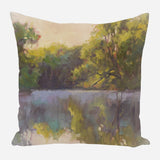 Decorative pillow featuring an impressionistic landscape of a creek with green trees and golden sunlight reflecting on calm water.
