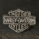 White neon sign shaped like the Harley Davidson shield with the words MOTOR, HARLEY DAVIDSON, and CYCLES illuminated against a black background.