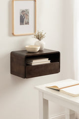 Dark brown wall-mounted side table with rounded edges, featuring an open shelf with books and a drawer, topped with a white bowl and vase with dried flowers.