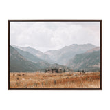 Framed canvas showing a wide valley with golden grasses in the foreground and layered blue-gray mountains under a cloudy sky in the background.