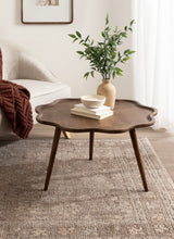 Dark wood scalloped coffee table with three tapered legs, decorated with a beige vase containing green leafy branches and a small bowl over stacked books.