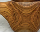 Close-up of a teak kuksa cup showing rich wood grain patterns and a smooth, rounded carving with a visible handle and hanging hole.
