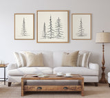 Three framed minimalist evergreen tree sketches in black on off-white canvas above a light gray sofa with beige and striped pillows, flanked by a wood side table and floor lamp.